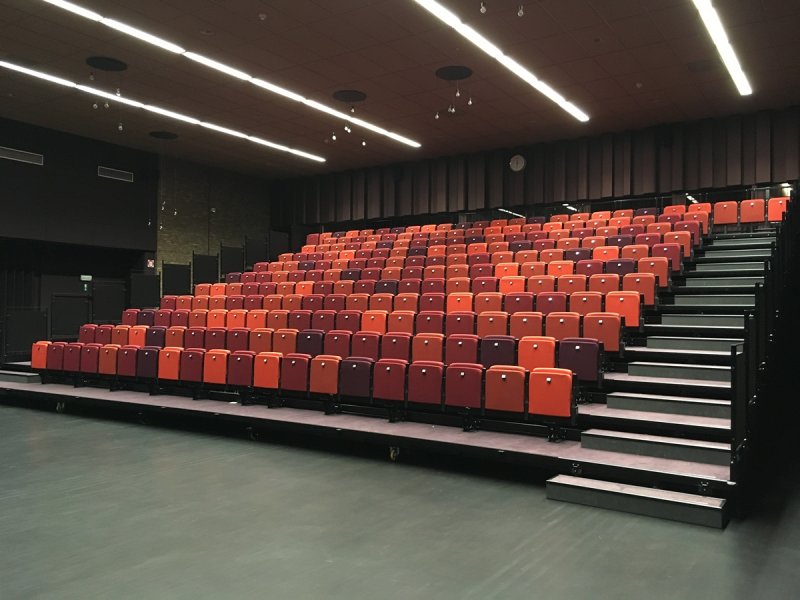 Telescopic grandstand with fully automatic chairs. Liniair movable in hall towards stage.